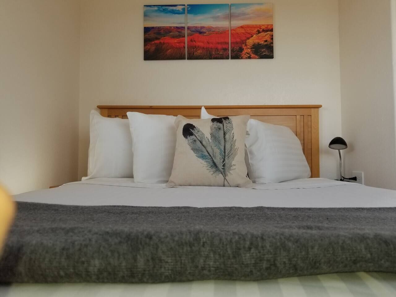 Una cama con ropa de cama blanca y una manta gris, un cabecero de madera y una mesita de noche con una lámpara.