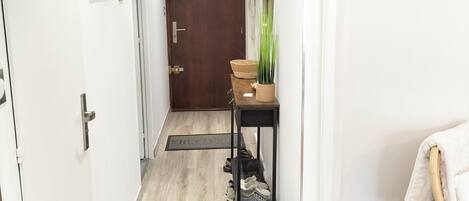 A hallway with a wooden floor, a door at the end, a small table with a plant, and a chair with a towel.