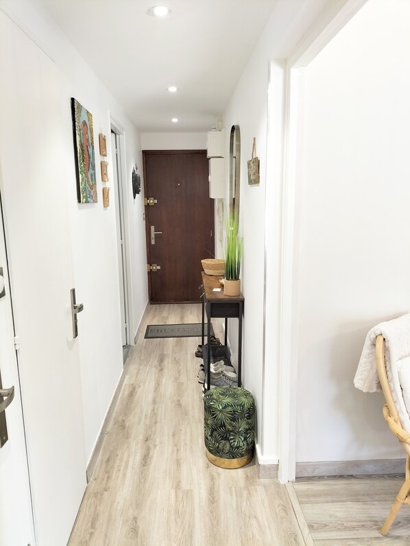 A hallway with a wooden floor, a door at the end, a small table with a plant, and a chair with a towel. - T2 Between the Sea and the Pond (Sète)