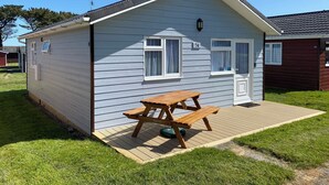 Ett litet, enplanshus på hjul med ett picknickbord framför, en liten veranda och en gräsig trädgård.