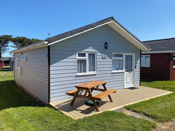 A small, single-story mobile home with a picnic table in front, a small deck, and a grassy yard.