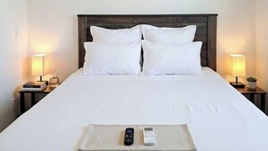 A hotel room with a bed, two bedside lamps, a ceiling fan, an air conditioner, and a bedside table with a book and a glass. - Grand Canyon Gateway-Cozy Private Mobile Home Suite w/ Full Kitchen (Williams)