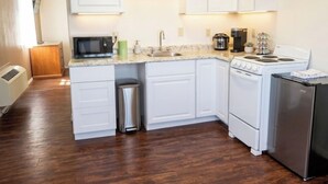 A kitchen with white cabinets, a microwave, a stove, a sink, and a trash can. - Grand Canyon Gateway-Cozy Private Mobile Home Suite w/ Full Kitchen (Williams)