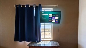 A room with a flat-screen TV mounted on the wall, a wooden cabinet, and a window with curtains. - Grand Canyon Gateway-Cozy Private Mobile Home Suite w/ Full Kitchen (Williams)