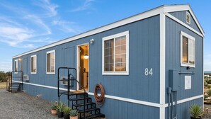 A single-story, blue building with a number '84' on the side, a door, and a small porch with steps and potted plants. - Grand Canyon Gateway-Cozy Private Mobile Home Suite w/ Full Kitchen (Williams)