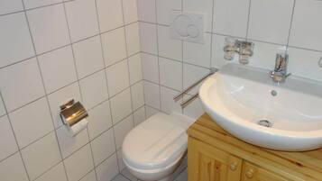 A small bathroom with a toilet, a sink, and a towel dispenser.