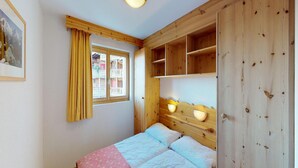 A bedroom with a wooden headboard, a bed with white and pink bedding, a window with yellow curtains, and a framed picture on the wall. - Apartment in Nendaz Near Ski Lift (Nendaz)