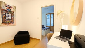 A modern room with a laptop on a desk, a black ottoman, a wall-mounted lamp, and a door leading to another room. - La Terrazza del Garraffello (Palermo)
