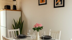 A dining table set for four with white chairs, a vase with pink flowers, and two framed pictures on the wall. - La Terrazza del Garraffello (Palermo)