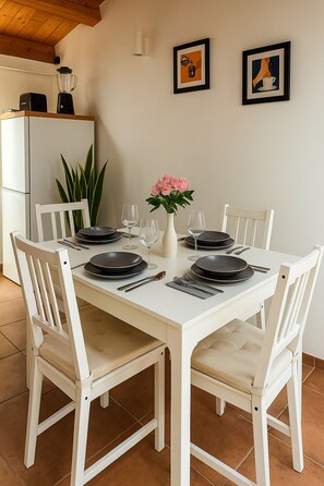 A dining table set for four with white chairs, a vase with pink flowers, and two framed pictures on the wall. - La Terrazza del Garraffello (Palermo)