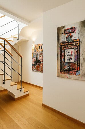 Un interior moderno con una escalera, suelo de madera y obras de arte en las paredes.