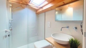 A modern bathroom with a glass shower enclosure, a white toilet, a wooden vanity with a white sink, and a small potted plant. - La Terrazza del Garraffello (Palermo)