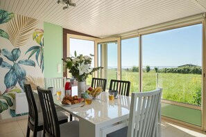 Ein Essbereich mit einem Tisch für vier Personen, einem Blumenstrauß und Blick auf ein grünes Feld durch große Fenster.