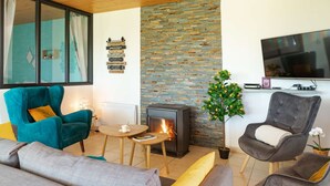 A living room with a fireplace, teal and gray chairs, a sofa, a TV, and a stone wall. - Magic Mountain breathtaking view of Mt Stmichel Bay (Dragey-Ronthon)