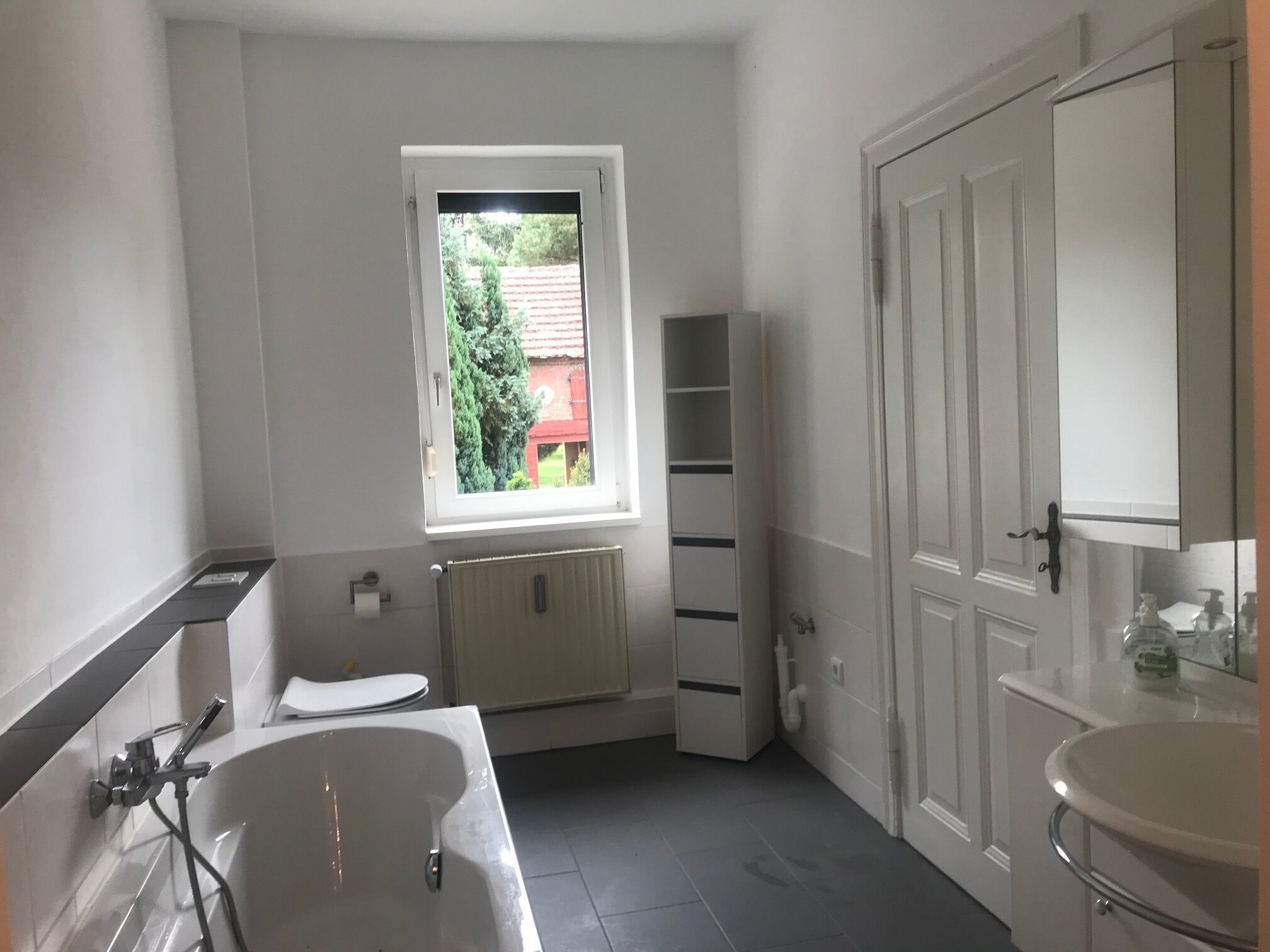 A modern bathroom with a bathtub, a window, a toilet, and a sink.