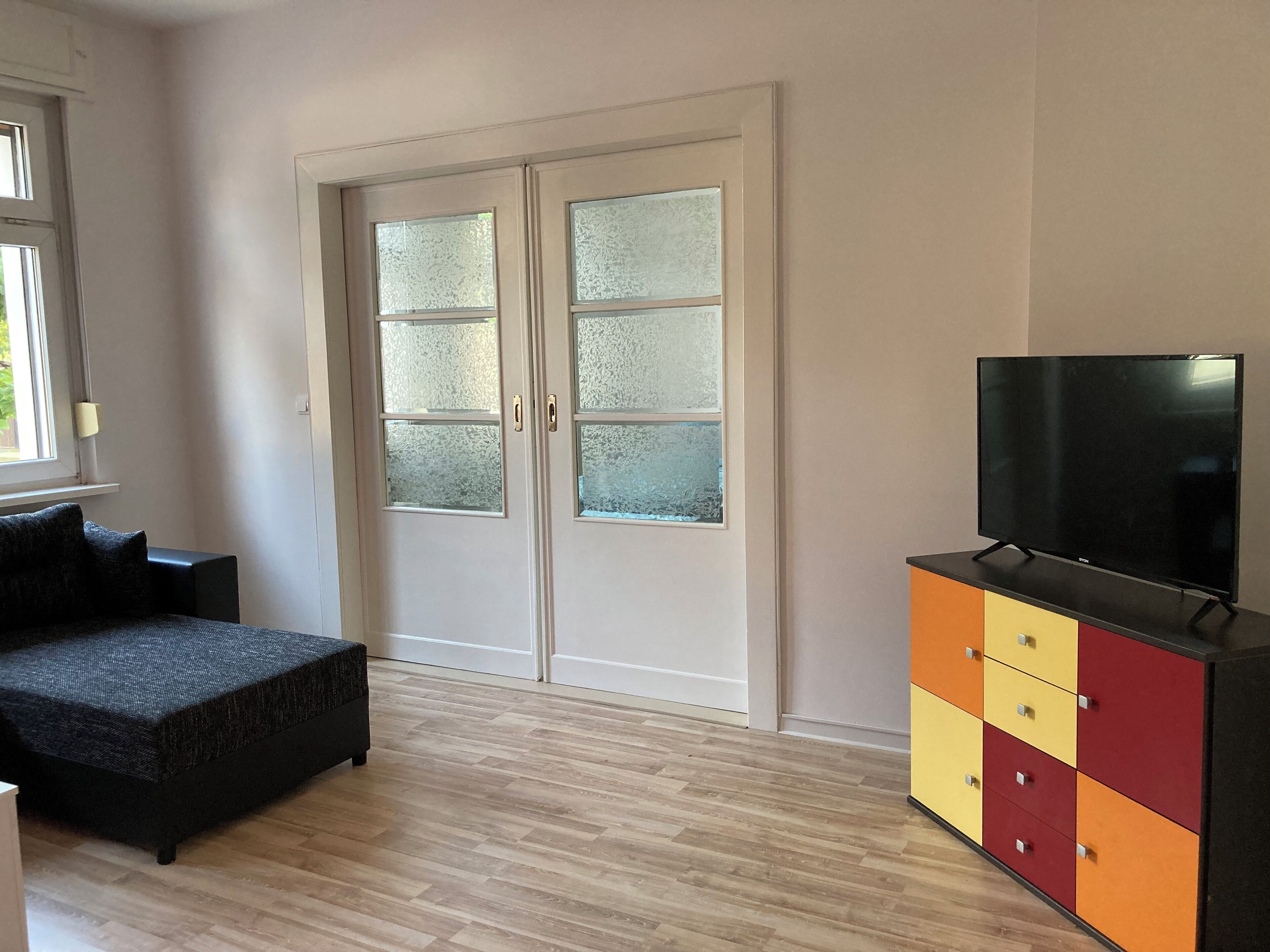 A bedroom with a bed, a TV on a cabinet, and frosted glass doors.