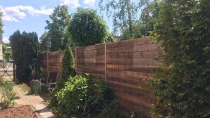 A wooden fence with a garden area in front, including a pathway and various plants. - 2-room apartment near Berlin, 72 sqm (Velten)