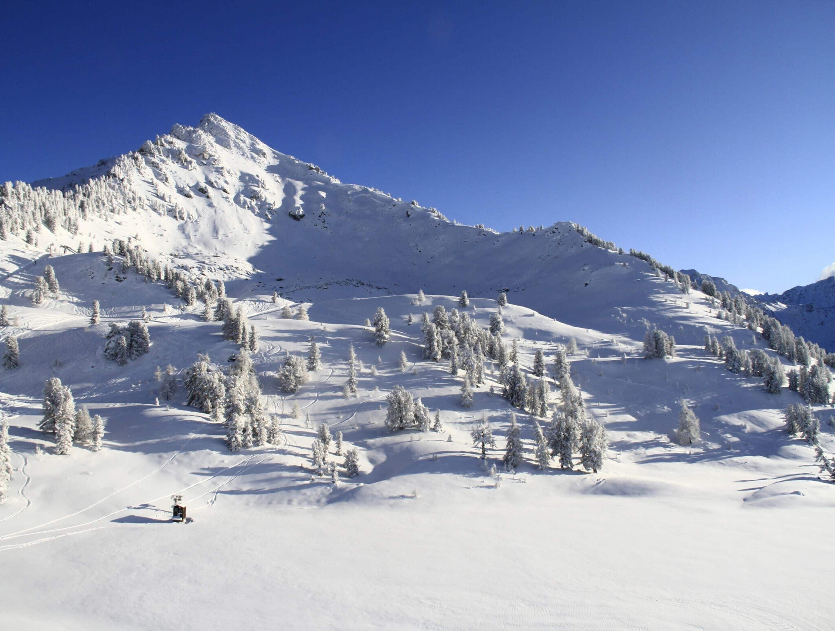 A snowy mountain landscape with a ski lift and trees.