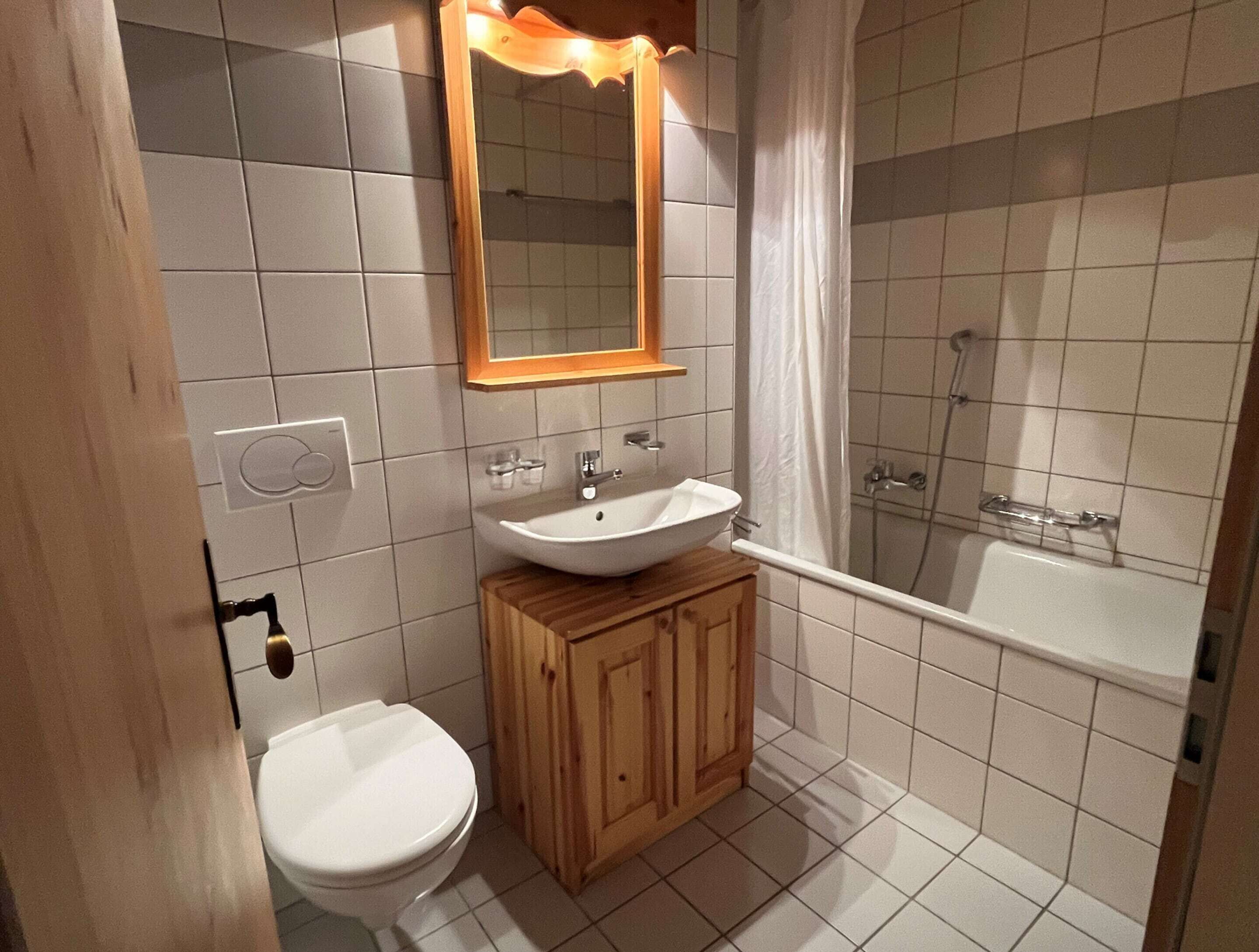 A bathroom with a white sink, wooden cabinet, white toilet, and a bathtub.
