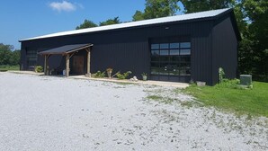 A modern building with a large garage door, a covered entrance, and a gravel driveway. - Cozy loft inside a vintage store on an animal rescue farm in Westville, IN (Westville)