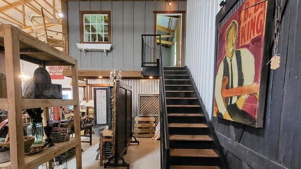 A staircase leading to a second floor in a building with a rustic interior, wooden beams, and a vintage poster on the wall. - Cozy loft inside a vintage store on an animal rescue farm in Westville, IN (Westville)