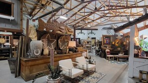 A spacious interior with high ceilings and exposed beams, featuring a central seating area with chairs and a coffee table, surrounded by various decorative items and furniture. - Cozy loft inside a vintage store on an animal rescue farm in Westville, IN (Westville)