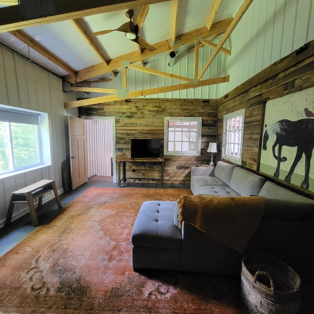 A rustic interior with a wooden ceiling, a sofa, a television, and a horse painting on the wall.