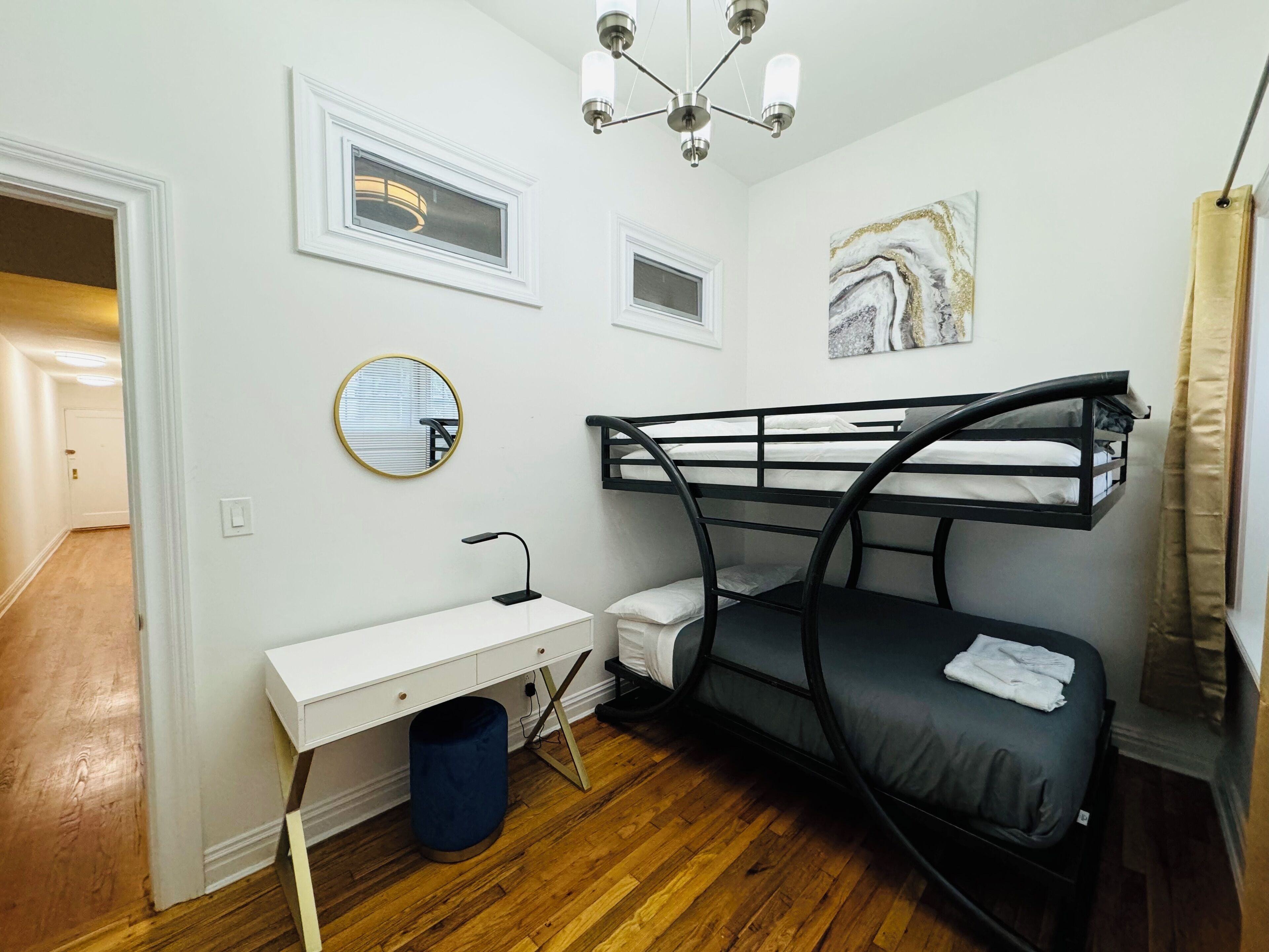 A compact room with a bunk bed, a small desk, a mirror, a ceiling light, and a marble artwork on the wall.