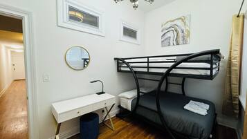 A compact room with a bunk bed, a small desk, a mirror, a ceiling light, and a marble artwork on the wall.