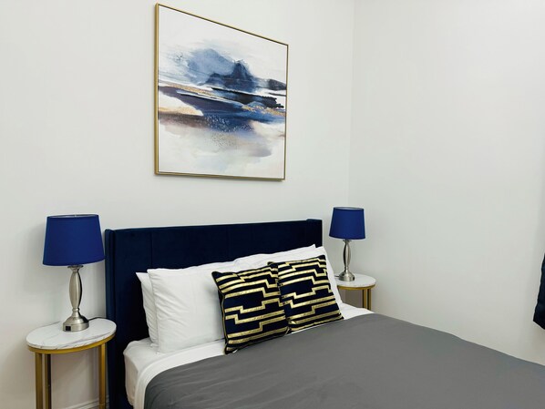 Une chambre à coucher bien rangée, avec un lit, deux tables de chevet et un tableau abstrait accroché au mur.
