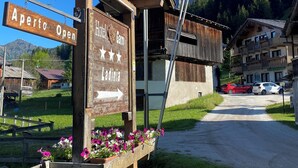 A wooden signpost with "Aperto Open" and "Hotel Carm Ladinia" directions, surrounded by flowers and flags.