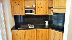 A compact kitchen with wooden cabinets, a black countertop, a microwave, a kettle, and two wooden chairs. - Flat in Nendaz Near Ski Slopes & Cable Cars (Nendaz)