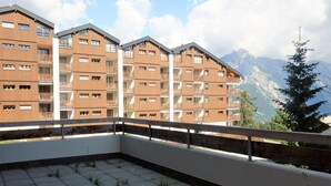 A balcony with a view of a mountain range, featuring a modern building with multiple balconies and a tiled floor. - Flat in Nendaz Near Ski Slopes & Cable Cars (Nendaz)