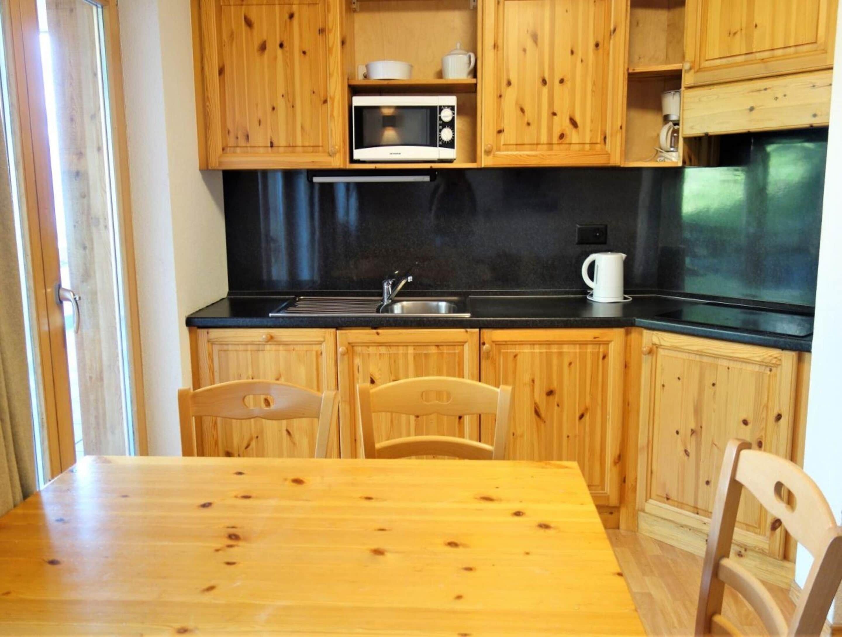 A kitchen with wooden cabinets, a black countertop, a microwave, a sink, and a dining table with chairs.