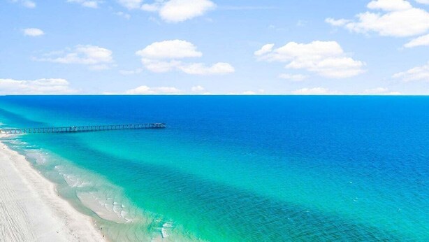 A beach with clear turquoise waters and a pier extending into the sea.