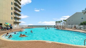 A swimming pool surrounded by a brick deck, with a building on one side and palm trees on the other.