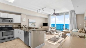 A modern kitchen with a central island, a dining area with a table and chairs, and a living room with a sofa and a TV.