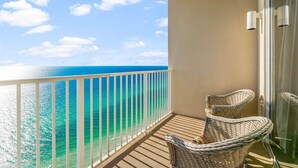 A balcony with a view of the ocean, wicker chairs, and a glass door.