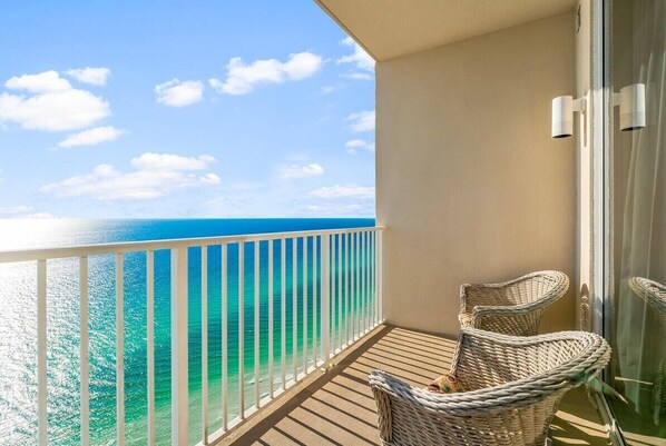 A balcony with a view of the ocean, wicker chairs, and a glass door.