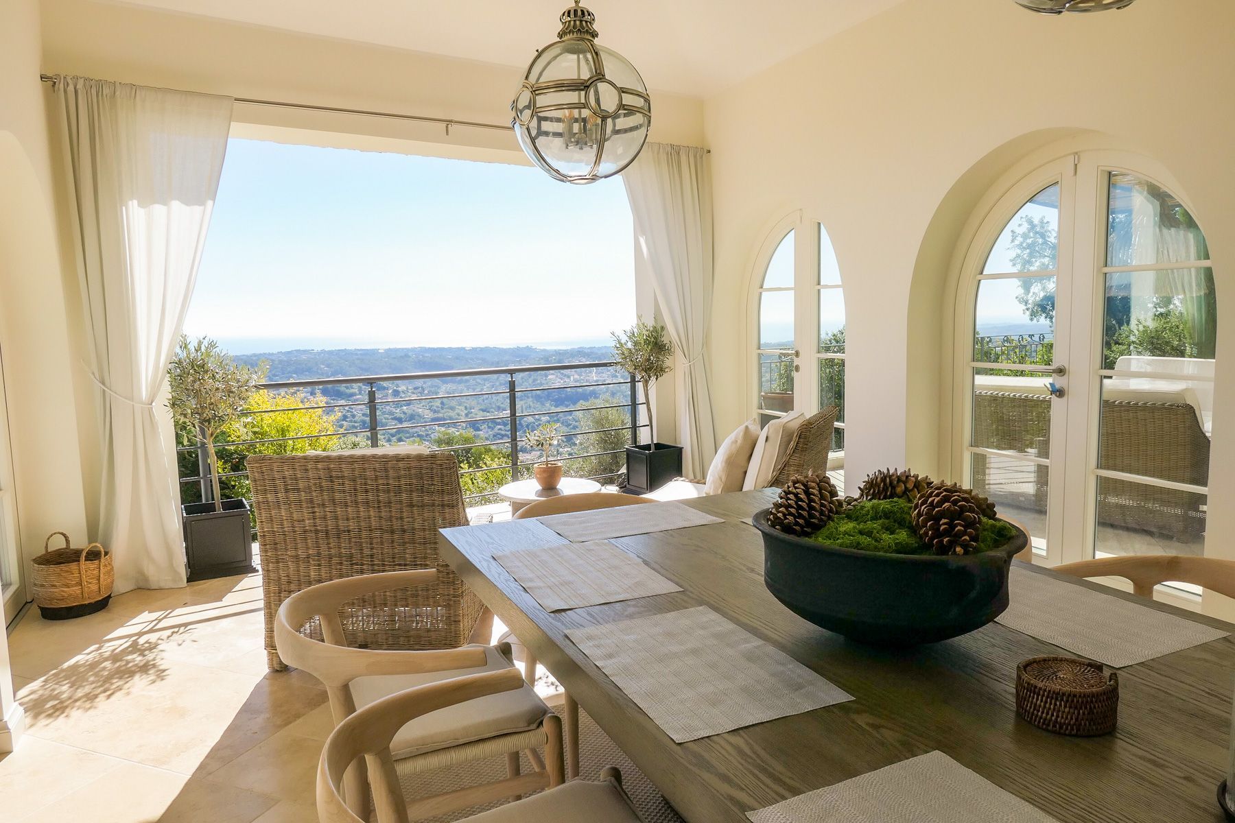 Un comedor con vistas al paisaje, muebles de mimbre y una mesa con piñas.