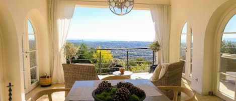 Un comedor con una mesa, sillas, una araña y vistas al paisaje.