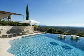 Une piscine privée, agrémentée de chaises longues et de parasols, entourée d’un mur de pierre et offrant une vue sur le paysage.