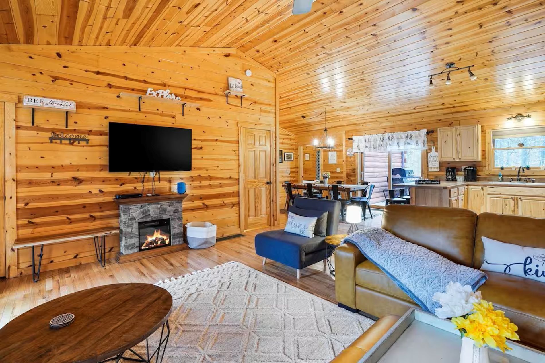 A cozy cabin interior with a fireplace, a television, a dining area, and a kitchen.