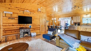 A cozy cabin interior with a fireplace, a television, a dining area, and a kitchen.