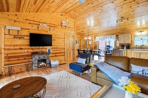 A cozy cabin interior with a fireplace, a television, a dining area, and a kitchen.
