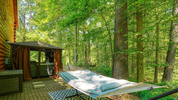 A hammock bed in a forested area with a wooden cabin and a small shed. - Honeybee Hideaway | Hot Tub, Game Room, Pond (Logan)