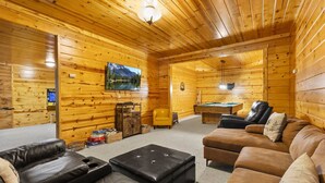 A cozy log cabin interior with a living room, a pool table, and a mounted television. - Honeybee Hideaway | Hot Tub, Game Room, Pond (Logan)