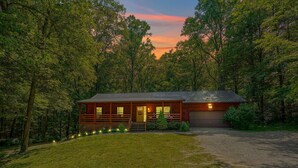 A cabin with a wooden exterior, a front porch, and a garage. - Honeybee Hideaway | Hot Tub, Game Room, Pond (Logan)
