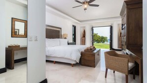 A bedroom with a bed, a wooden nightstand, a wicker chair, a ceiling fan, and a view of the outdoors.