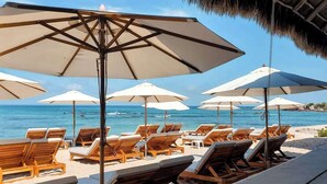 A beachside lounge area with wooden lounge chairs and large umbrellas, overlooking the ocean.